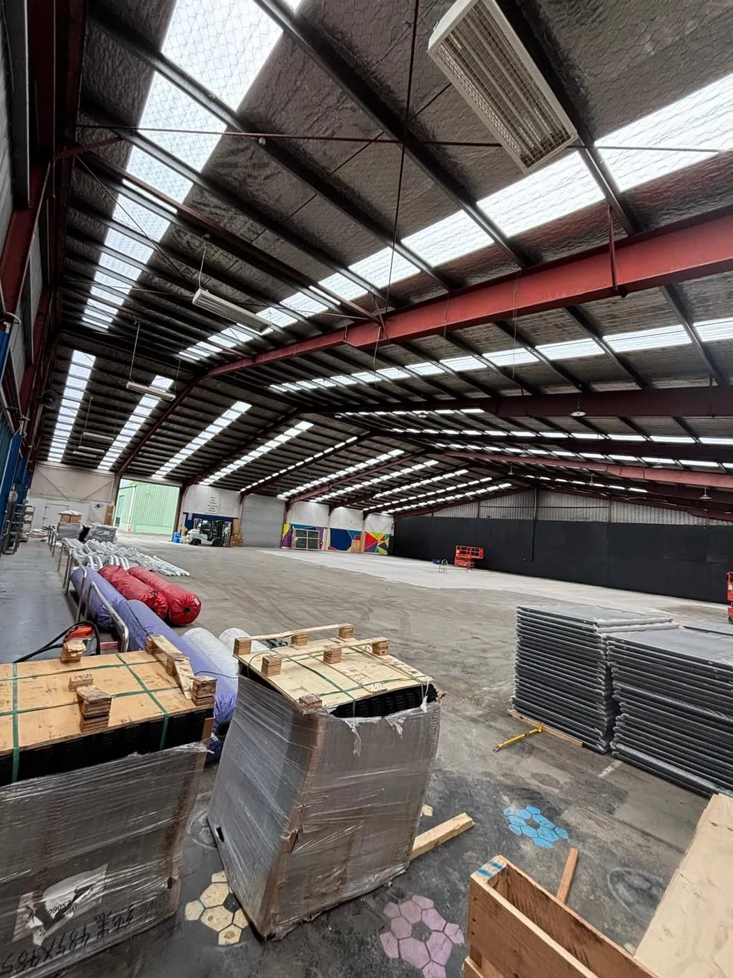 A huge empty warehouse with pallets of court parts and rolls of turf