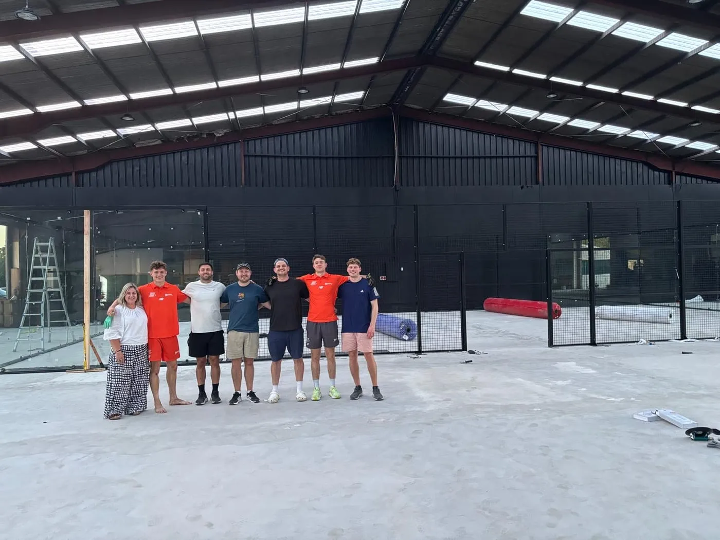 Seven people standing arm in arm on the bare floor in front of the new court frames