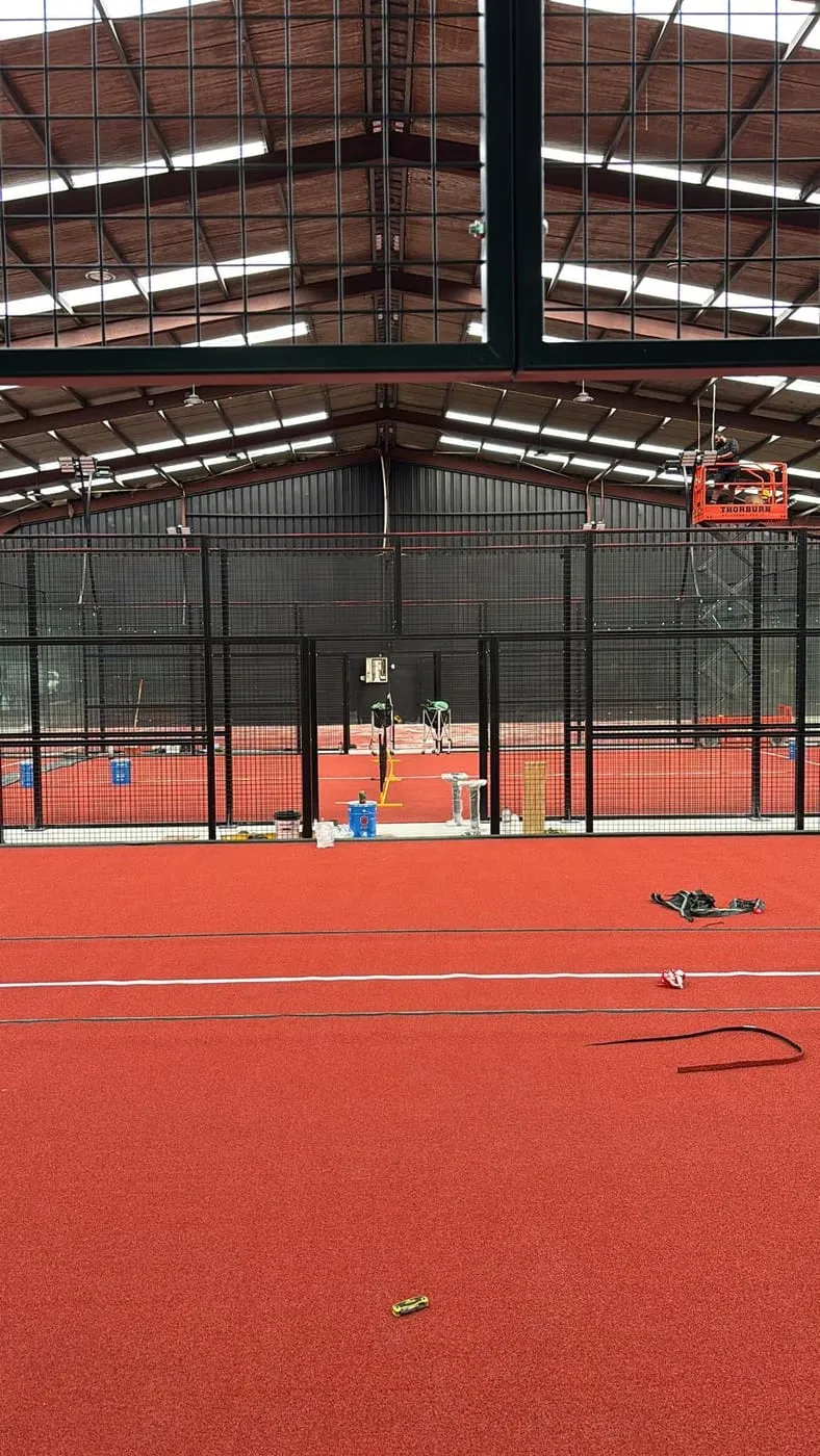 New red turf being laid on a Padel Park court, with a scissor lift by the glass
