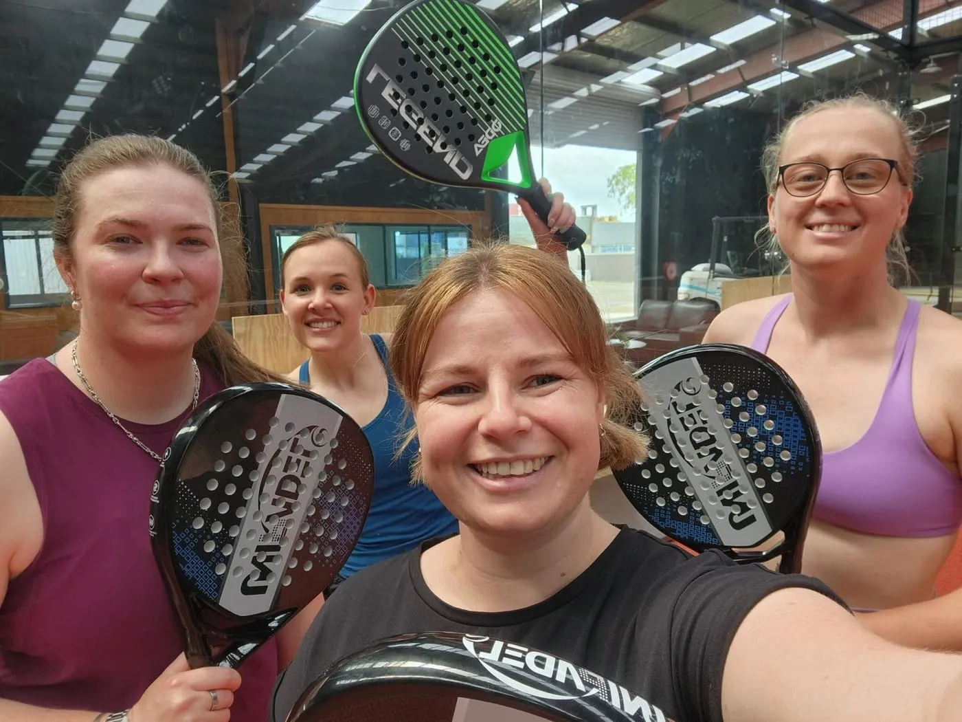 Four smiling players holding up their padel rackets on court