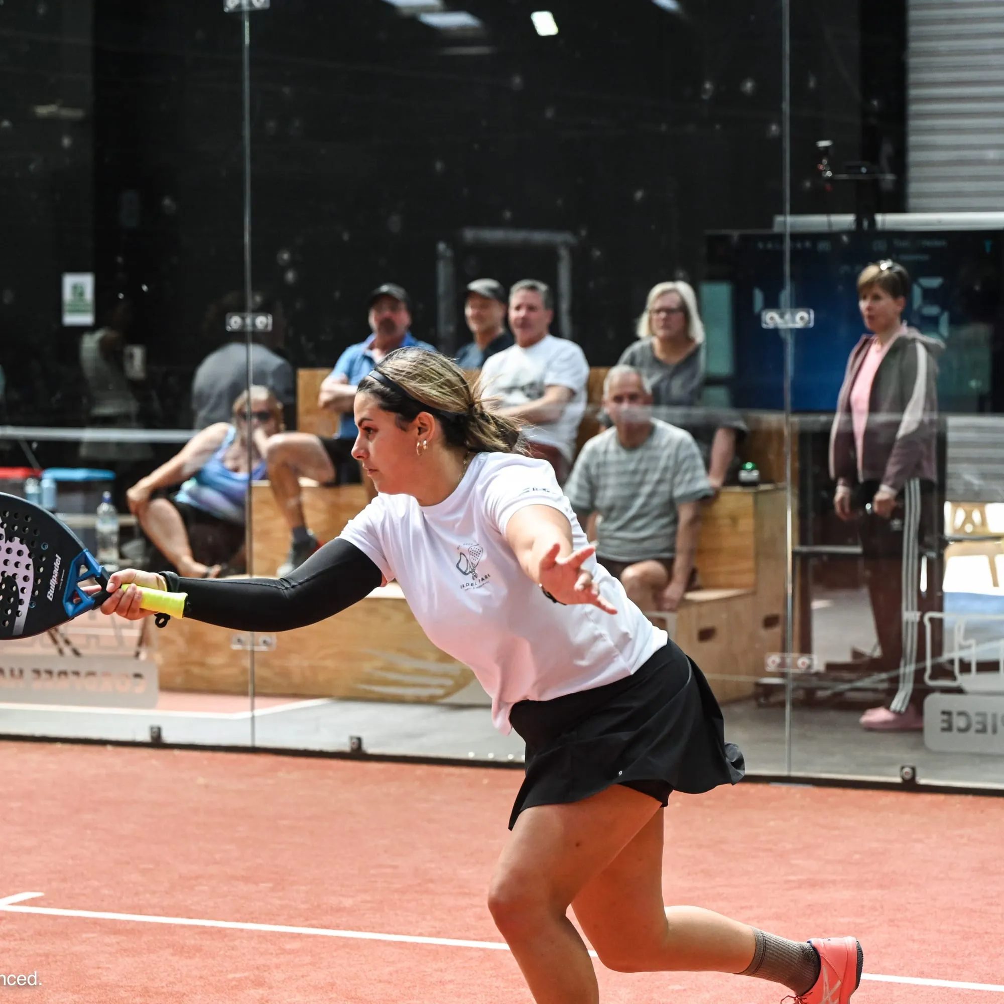 A padel player stretching wide for a forehand